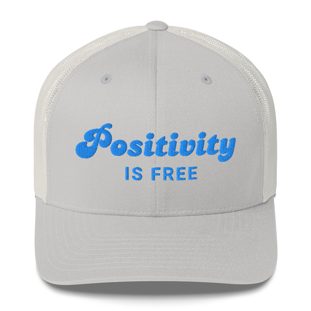 A silver trucker hat with the writng 'Positivity is free' in light blue embroidery.